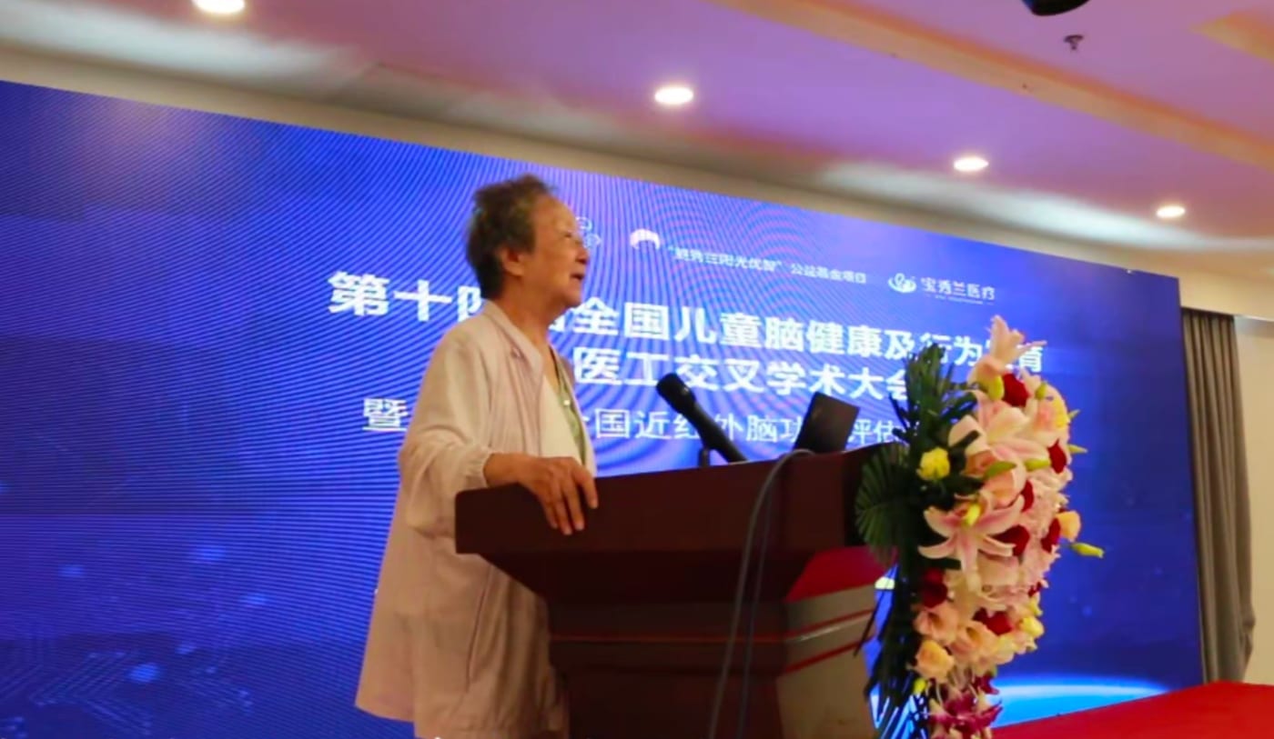 鲍秀兰教授站在讲台前致辞,身后背景板写着「第十四届全国儿童脑健康及行为发育医工交叉学术大会」
