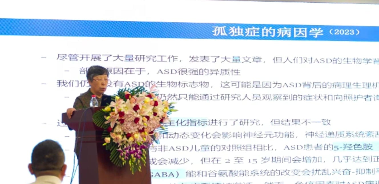 贾美香教授在讲台后作报告,幻灯片标题为「孤独症的病因学(2023)」