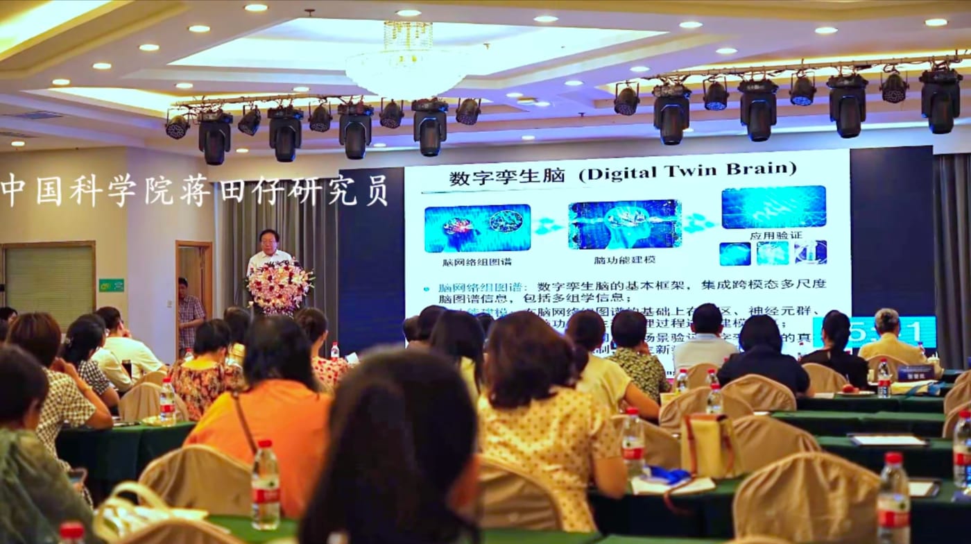蒋田仔研究员在讲台前作报告,大屏幻灯片标题为「数字孪生脑(Digital Twin Brain)」,前排坐满听众