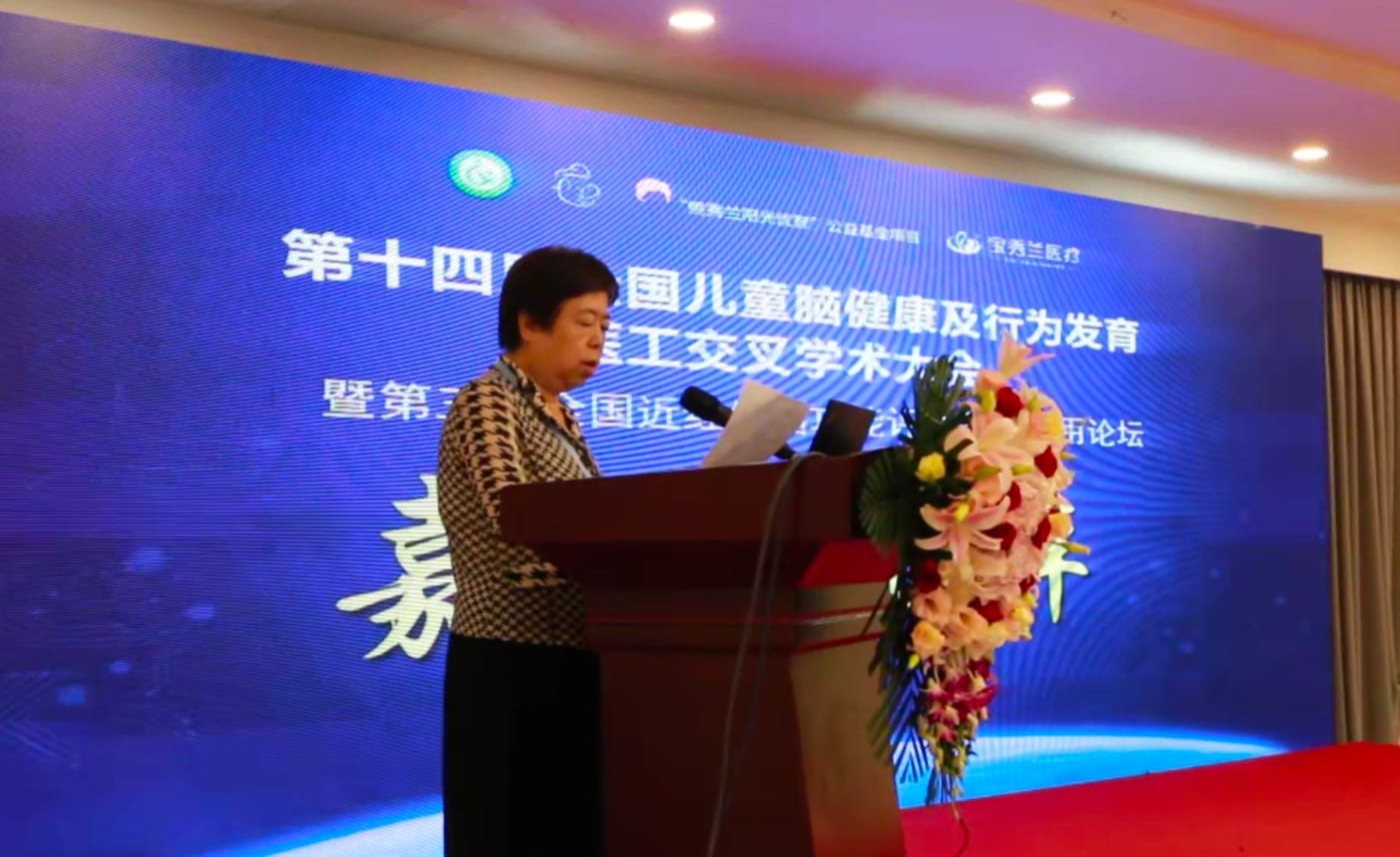 孙淑英教授站在讲台后拿着讲稿致辞,身后是大会背景板