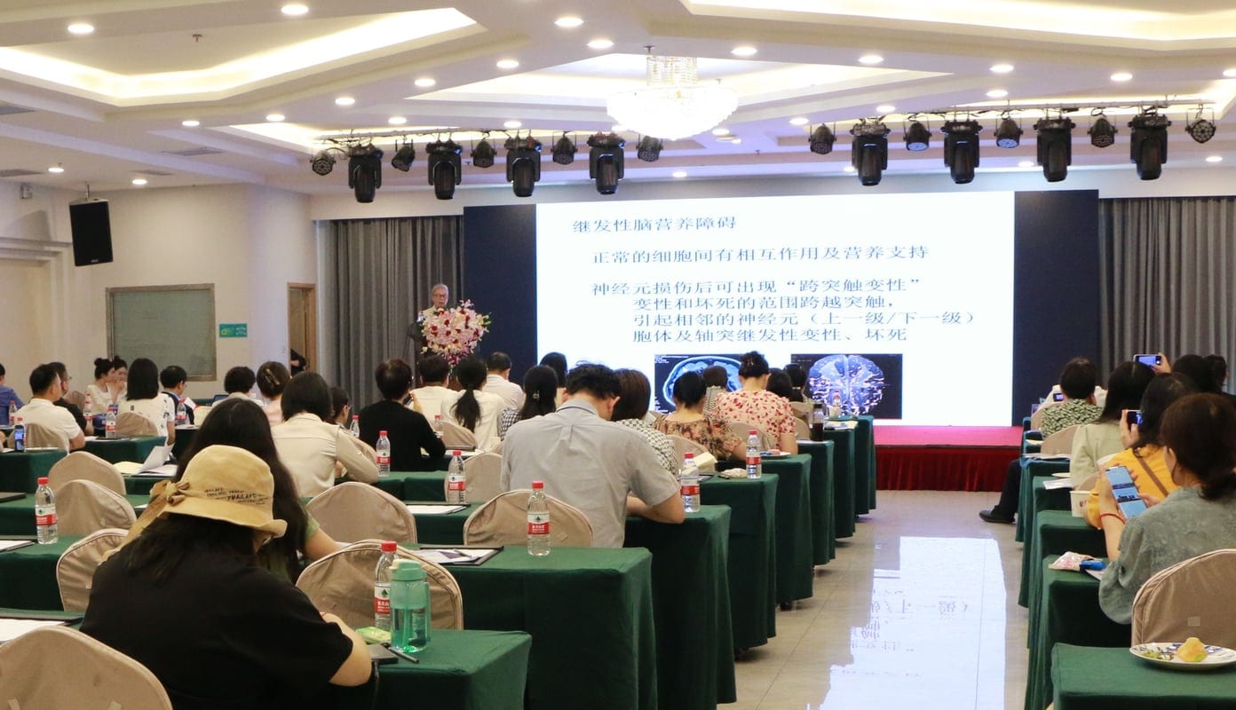 周丛乐教授在会场前方讲台作报告,大屏上是幻灯片,会场里坐满听众