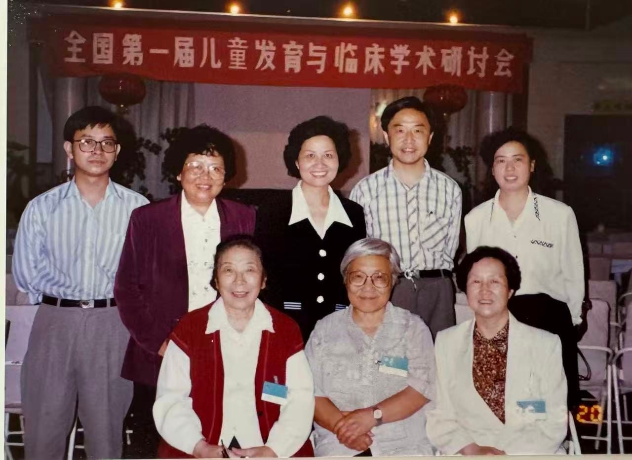 八人在会场合影，前排三人坐着，后排五人站立，身后横幅写着「全国第一届儿童发育与临床学术研讨会」