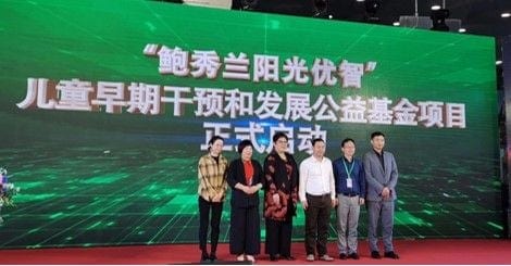 六人站在舞台上合影,身后大屏写着「「鲍秀兰阳光优智」儿童早期干预和发展公益基金项目正式启动」