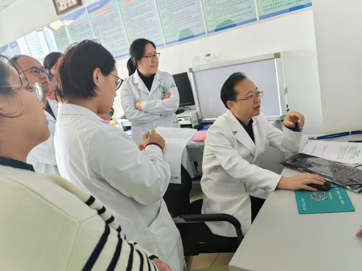 刘维民身穿白大褂坐在诊桌前讲解,几位医护人员站在一旁看屏幕、做记录
