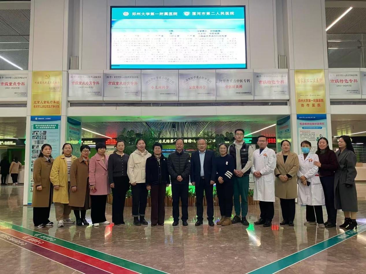 十余人在医院大厅里合影,身后挂着各级重点专科的牌匾与显示屏