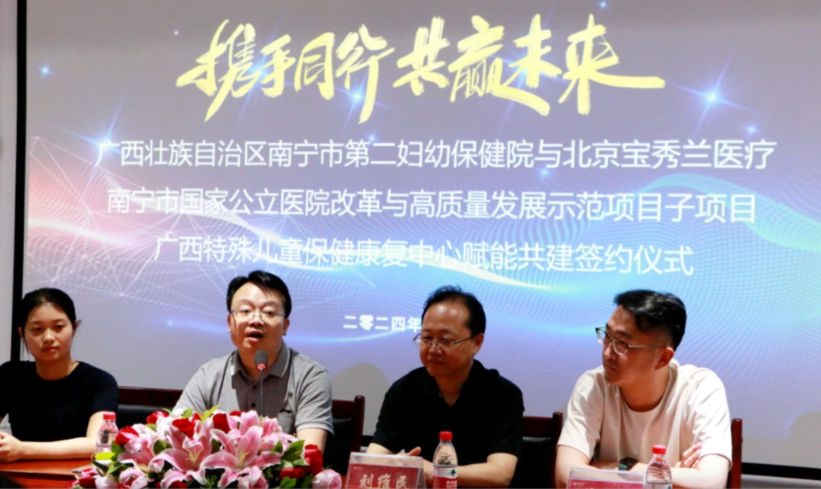 四人坐在主席台后,背景屏写着「南宁市第二妇幼保健院与北京宝秀兰医疗 广西特殊儿童保健康复中心赋能共建签约仪式」,桌上放着「刘维民」的桌牌