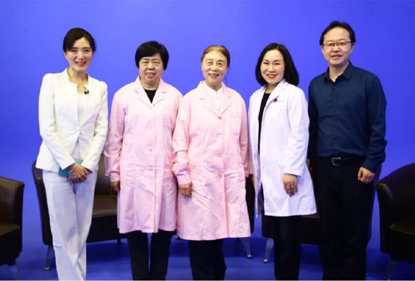 五人站在蓝色背景的演播室里合影,中间两位身穿粉色工作服,右侧一位是刘维民
