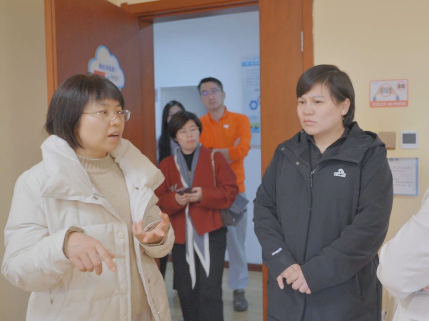 一位女士在训练室门口向来访者介绍,几位来访者站在后面听