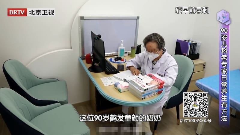 电视节目画面：鲍秀兰教授穿白大褂坐在诊室的桌前翻看资料